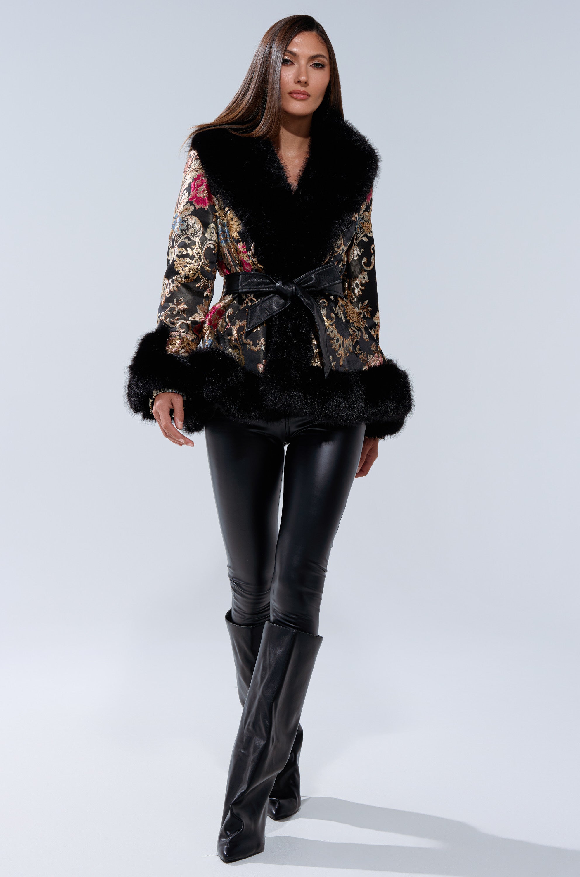 Wearing the KENZY LUXE FUR TRIM MOTO jacket with a belted waist, black leather pants, and tall black boots, a woman walks confidently against a plain light background.