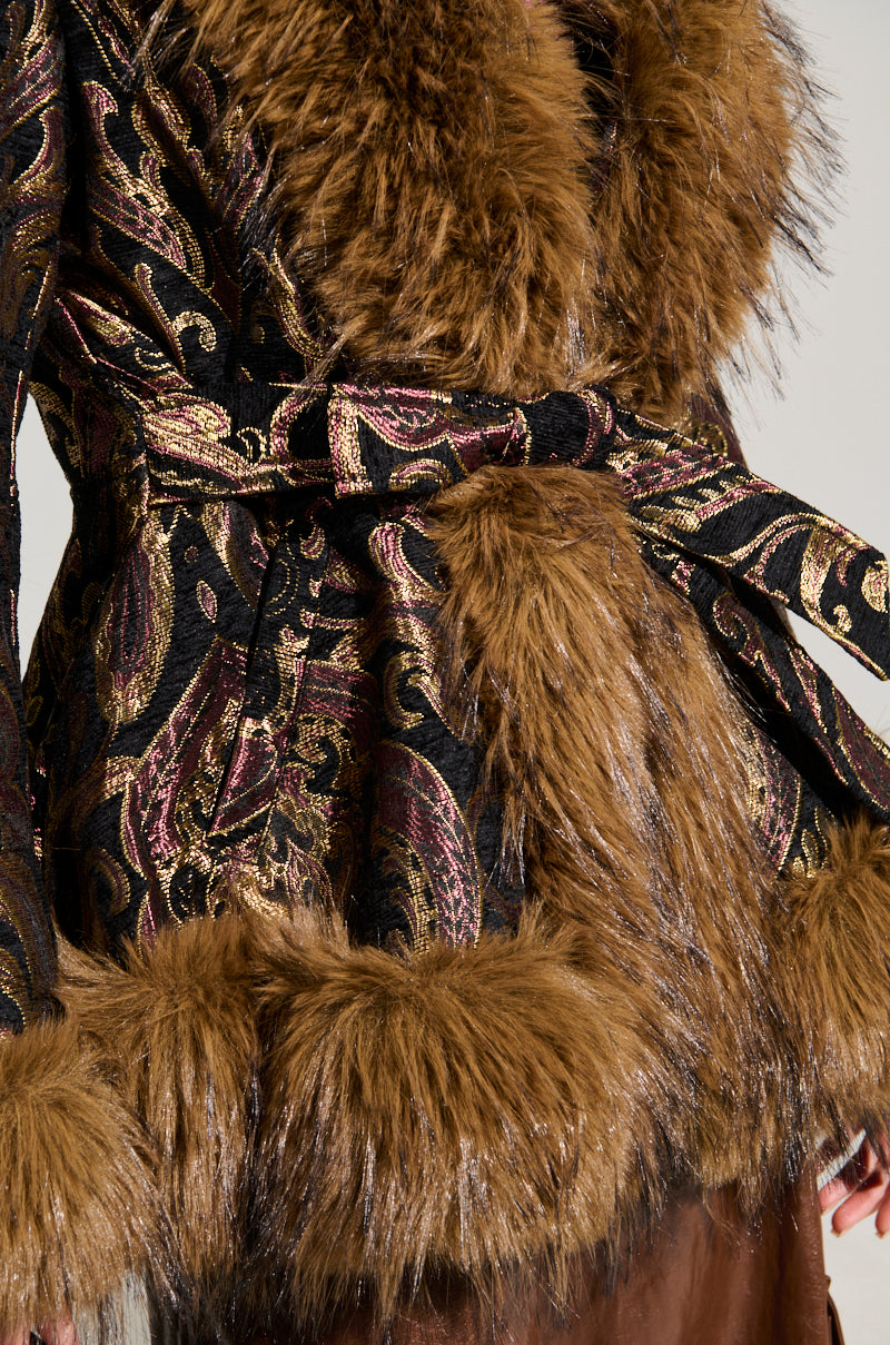 Close-up of the SITTING PRETTY FUR TRIM COAT, featuring intricate gold and burgundy patterns on ornate velvet. This luxurious coat is highlighted by plush brown fur trim, a matching fur belt, and faux fur cuffs, creating a textured and elegant appearance.