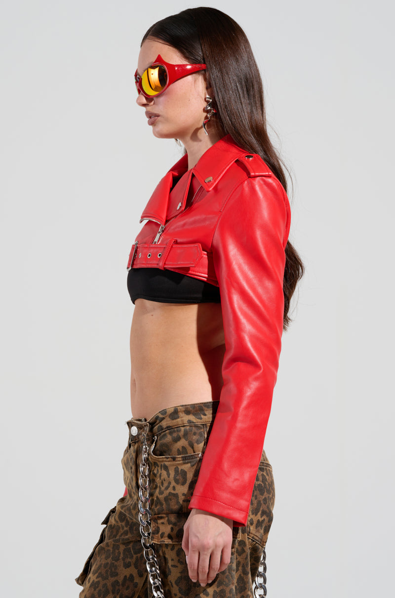 A person with long dark hair is wearing a red HALF MY HEART ULTRA CROP MOTO top, reflective sunglasses, and leopard print pants with an adjustable waist belt. Their profile is shown against a plain background.