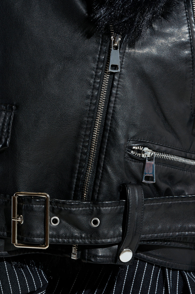 Close-up of the ON THE GO FUR TRIM MOTO in black, showcasing metal zippers, a belt with a silver buckle, and buttons. The prominent texture of the faux leather suggests a quilted interior lining beneath it.