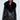 A person wearing the ON THE GO FUR TRIM MOTO IN BLACK, showcasing its chic faux leather design with a large faux fur collar, stylish zippers, and belt buckle detail. They're also sporting black sunglasses and a pinstriped outfit underneath, set against a plain, light-colored background.