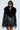 A person wearing the ON THE GO FUR TRIM MOTO IN BLACK, showcasing its chic faux leather design with a large faux fur collar, stylish zippers, and belt buckle detail. They're also sporting black sunglasses and a pinstriped outfit underneath, set against a plain, light-colored background.