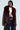 A person wearing the "ON THE GO FUR TRIM MOTO IN BURGUNDY," a jacket crafted from burgundy faux leather and featuring a prominent faux fur collar, paired with a white shirt and pinstriped pants. The ensemble is completed with a chain belt, set against a plain, light-hued backdrop.