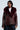 A person is wearing the fashionable "ON THE GO FUR TRIM MOTO IN BURGUNDY," a dark burgundy faux leather jacket with a large faux fur collar, multiple zippers, and a belt. They have shoulder-length hair and are standing against a plain background.