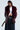 Confidently standing against a simple light background, a person wears the "ON THE GO FUR TRIM MOTO IN BURGUNDY" over a white shirt and dark pinstripe pants. The chic look is completed with a pearl belt and a stylish, short dark hairstyle, emanating an effortlessly cool vibe.