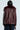 A person stands facing away, wearing the 'ON THE GO FUR TRIM MOTO IN BURGUNDY,' a dark brown jacket featuring a dark red faux fur collar. The jacket is paired with dark pants against a plain light background.