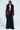 A person stands confidently on a neutral background, showcasing a stylish outfit that highlights the ON THE GO FUR TRIM MOTO IN BURGUNDY, paired with a cropped white shirt and wide-leg pinstripe pants.