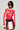 Wearing the REV IT UP RACING MOTO IN RED jacket, featuring a striking combination of vibrant red and white hues along with an array of logos, they perfectly pair it with a matching skirt. With short dark hair and dark sunglasses, they exude confidence against a plain backdrop.