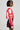 A person wearing sunglasses stands in profile against a plain background, sporting the REV IT UP RACING MOTO IN RED jacket. This faux leather outerwear features bold and dynamic racing-inspired embroidered patches, including the word 