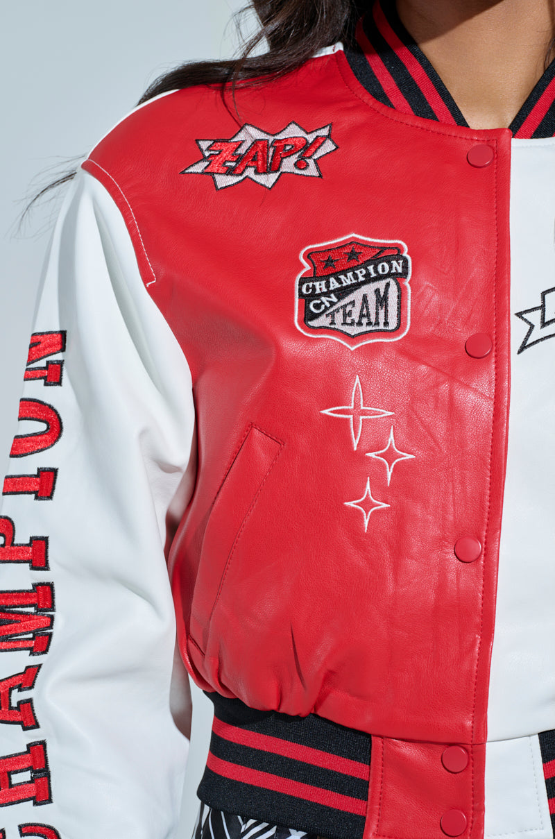 Close-up of someone in the Champions League Faux Leather Bomber, a red and white varsity jacket with sports-themed patches. "Champion Team," "Zap!" and star designs adorn this color-block bomber as they stand against a light background, partially visible from the shoulder down.