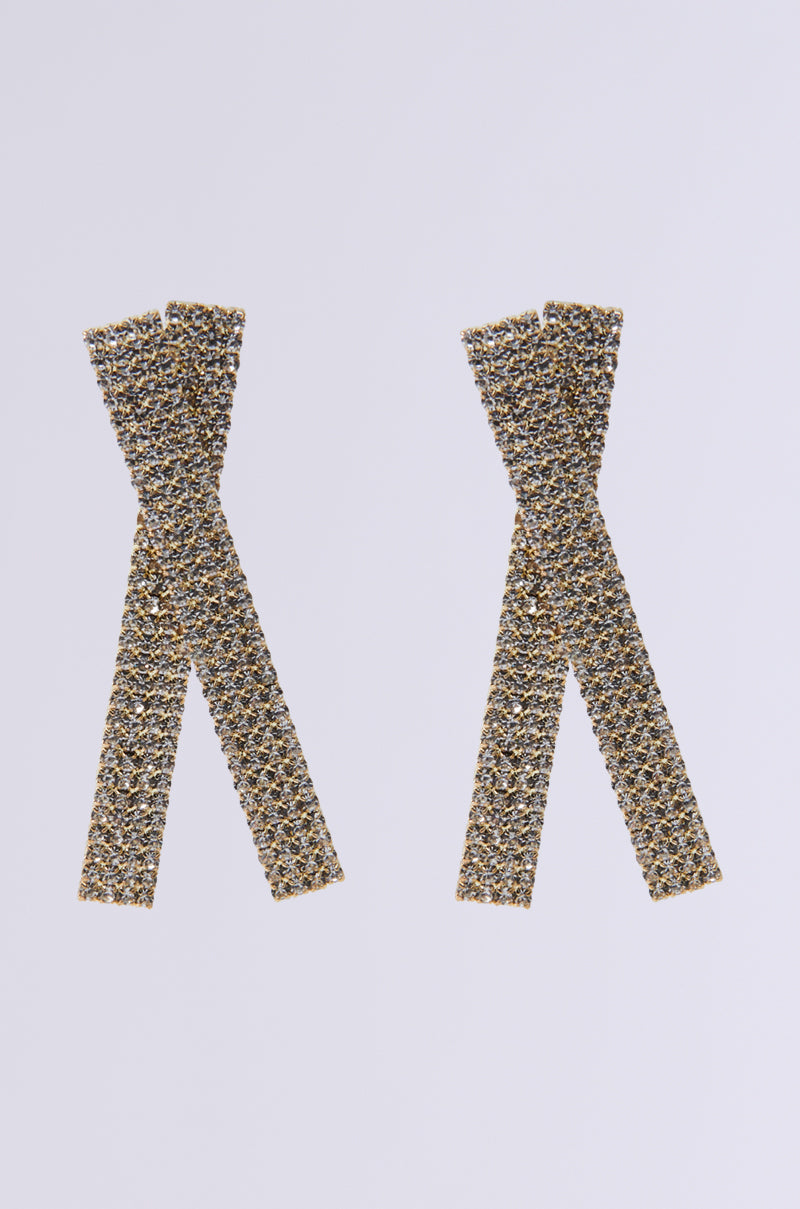 The CROSS OUT BLING EARRING, featuring faux gold and textured ribbon shapes adorned with pave rhinestones, sparkles elegantly against a plain white background.