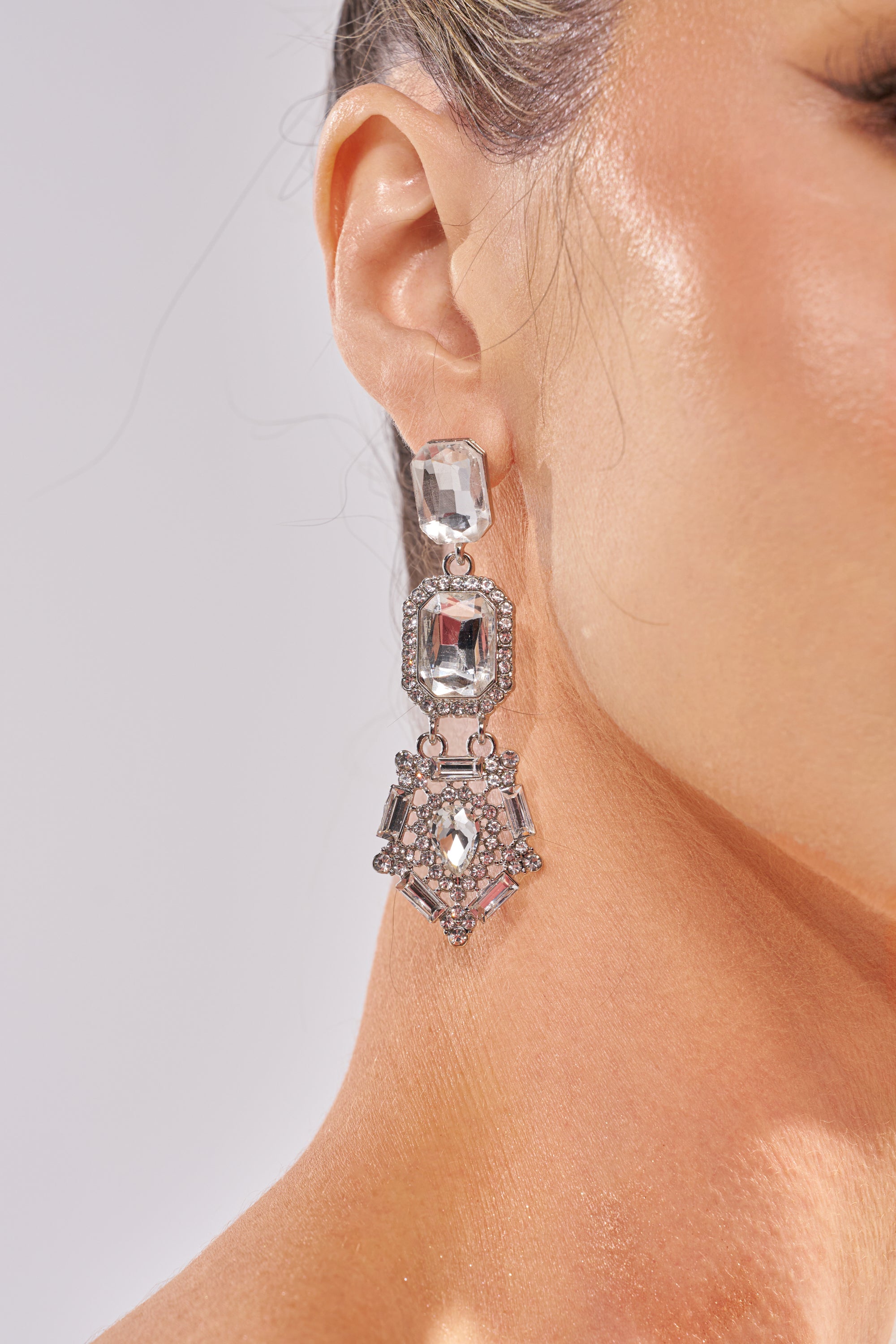 Close-up of a woman's ear wearing ART DECO EARRING, featuring multiple large faceted clear crystals in geometric shapes set in an ornate design—perfect statement earrings for formal occasions. 1