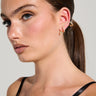 A woman with long, dark hair in a sleek ponytail is wearing a black strappy top. Her ear is adorned with a metallic faux gold snake-shaped cuff and the COUTURE WRAP EARRING, which adds an elegant touch. The light-colored, plain background accentuates her chic accessories.