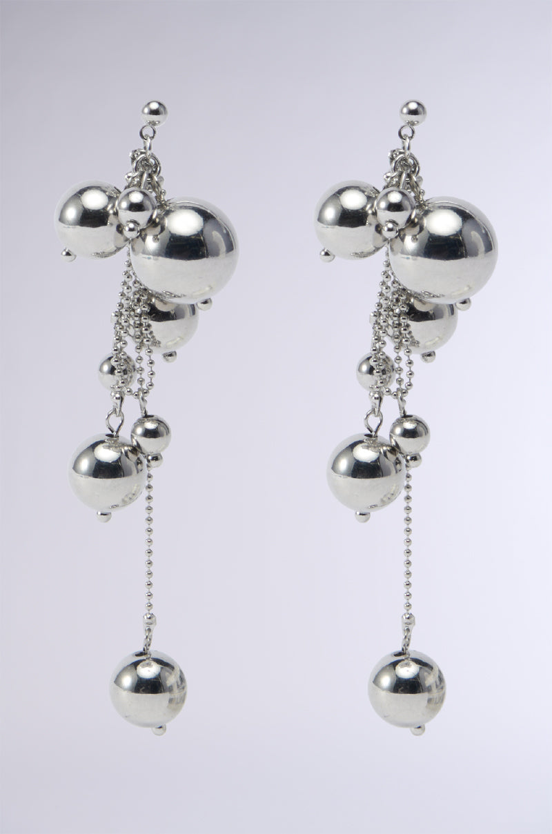 The BUBBLY DANGLE EARRING showcases metallic faux silver spheres of varying sizes, enhanced by chain link attachments that create a cascading effect against a plain, light gray background.