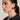 A woman with sleek, dark hair tied back is wearing large, rectangular MOD EARRING in metallic faux silver and a sparkling floral necklace. She is dressed in a black top with small white text. The background remains neutral, enhancing her minimalist design.
