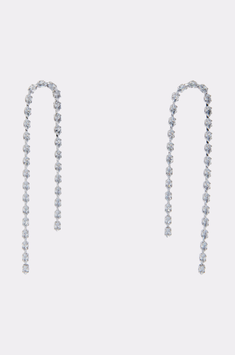 The WATERFALL DANGLE EARRING IN SILVER features delicate curved threader design with a row of small sparkling gemstones, creating a chic metallic accessory displayed against a plain white background. 1