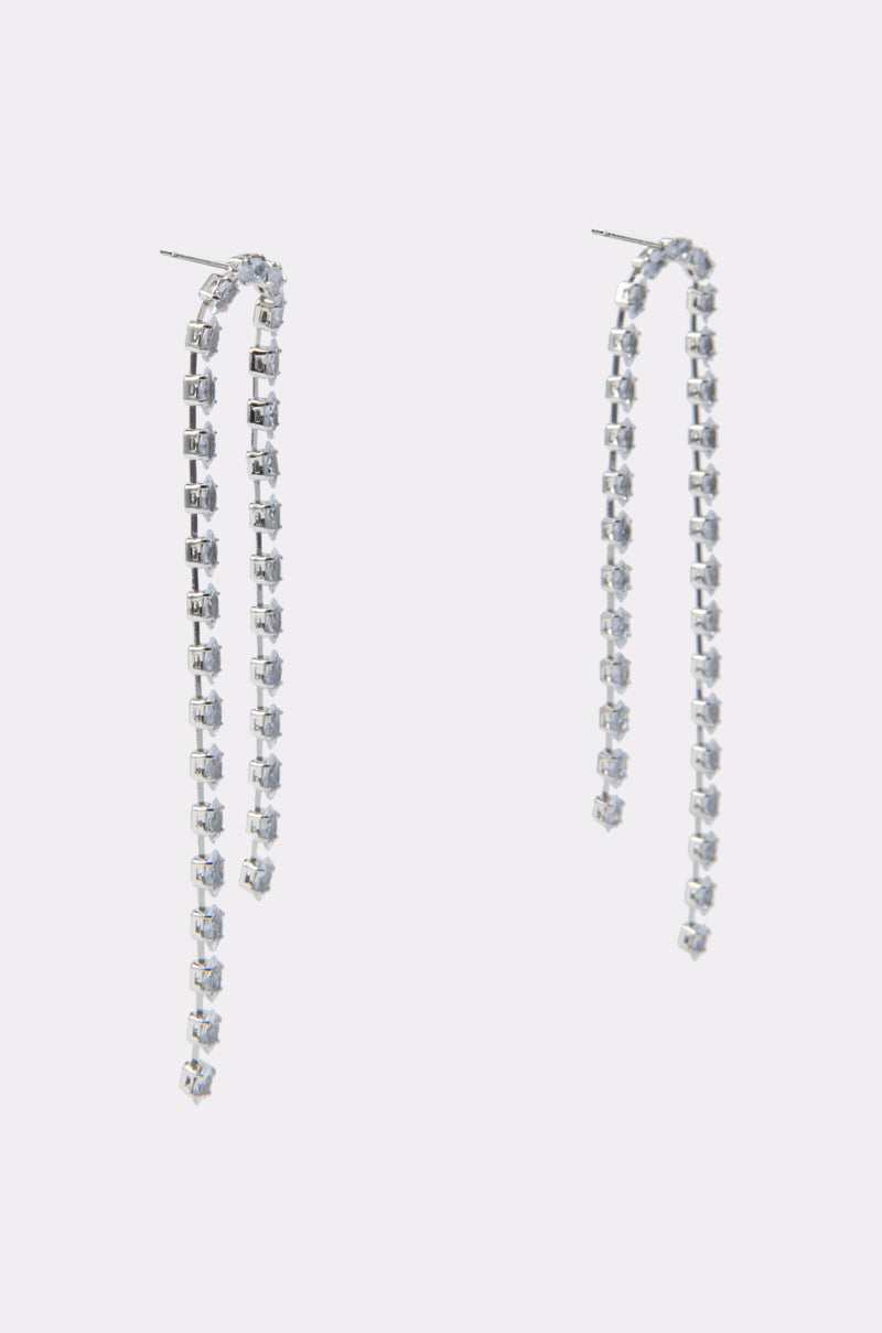 The WATERFALL DANGLE EARRING IN SILVER features long, metallic drop earrings with small, square clear gemstones and elegant rhinestone chain links, displayed on a plain light gray background. 3