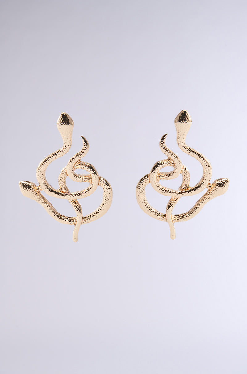 The WATCH YA STEP EARRING by AKIRA Label features two intricately designed faux gold earrings shaped like twisted snakes. Each showcases a detailed snake pattern with curves and points, set against a plain gray background, embodying a symmetrical and elegant appearance. 1