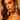 A woman with wavy brown hair confidently gazes into the camera, wearing the CHANDELIER DROP EARRING and a strapless red top against a warm, neutral background.
