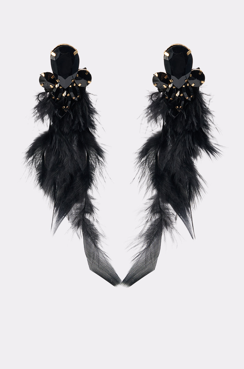 The SHOW ME EARRING is a pair of statement earrings with large black gemstones, black feather accents, and long sheer black fabric tassels, shown on a light background. 2