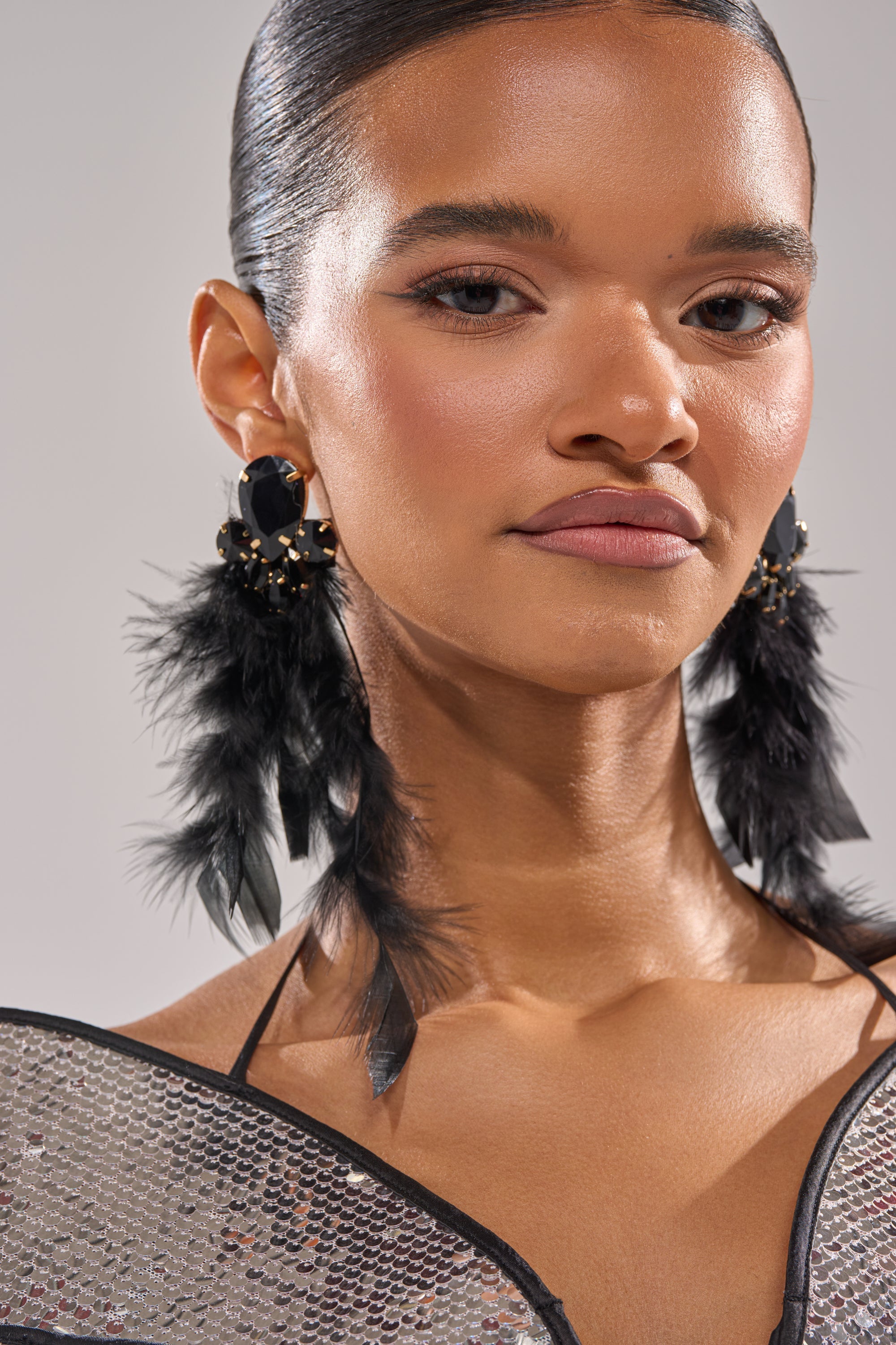 A woman with smooth, dark hair pulled back wears SHOW ME EARRING and a sparkling, silver-sequined top as she looks confidently at the camera against a neutral background. 0