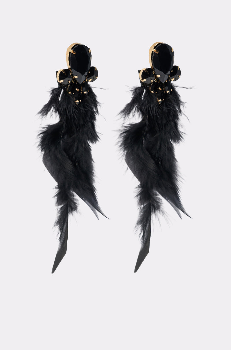 The SHOW ME EARRING pair features oversized crystals, gold accents, decorative bows, and long black feathers, all set against a plain white background. 3