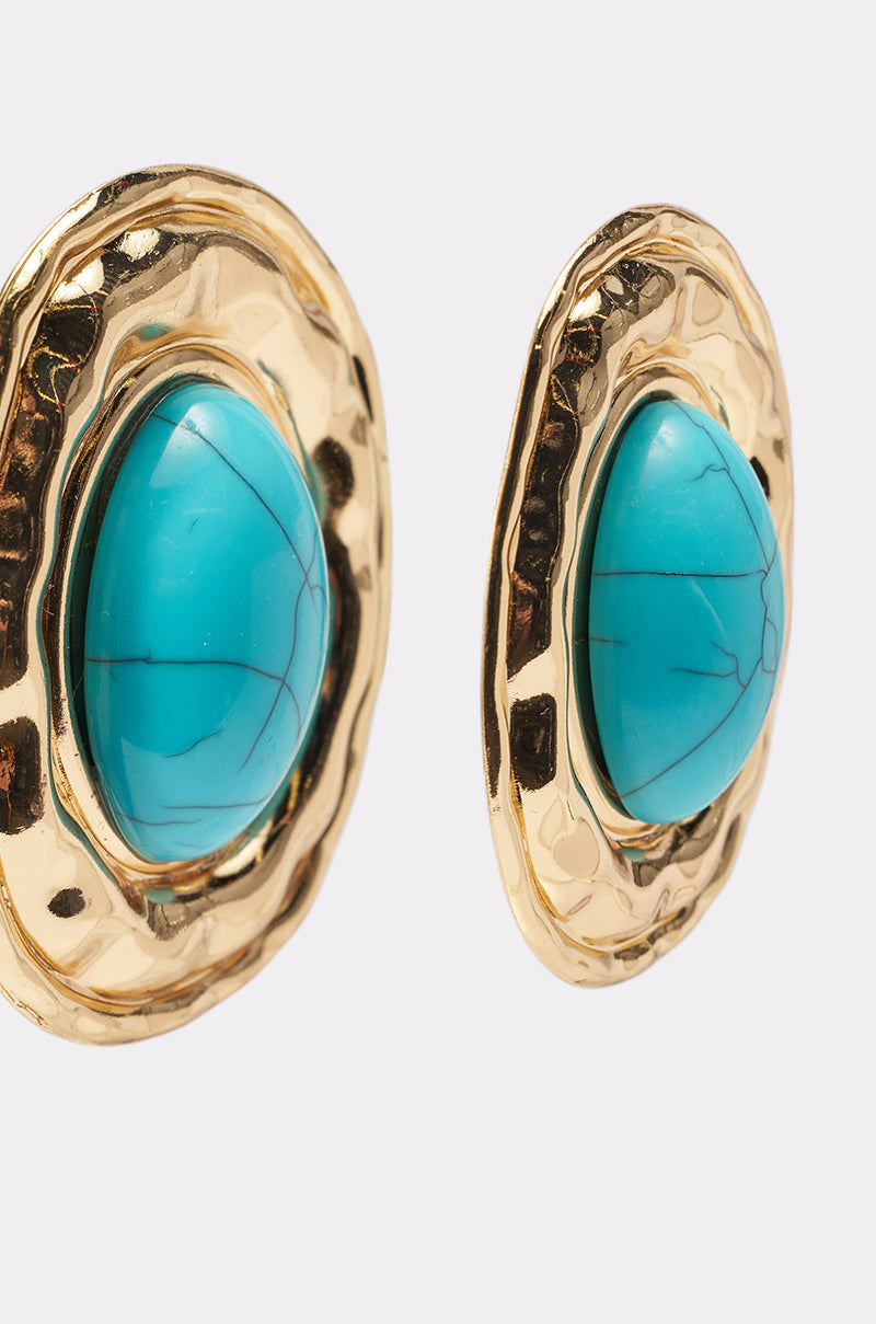 Close-up of the LONDON EARRING: two boho-chic earrings with a hammered gold texture, each set with a large oval turquoise stone in the center, displayed on a plain white background. 3