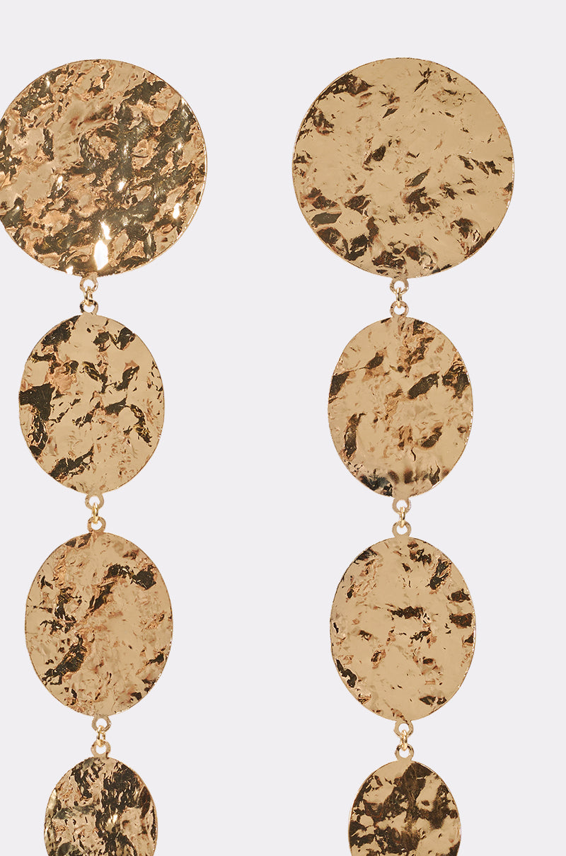 Close-up of the IN THE SUN EARRING featuring multiple gold hammered discs linked vertically, ideal as vacation accessories, shown against a plain light background. 3