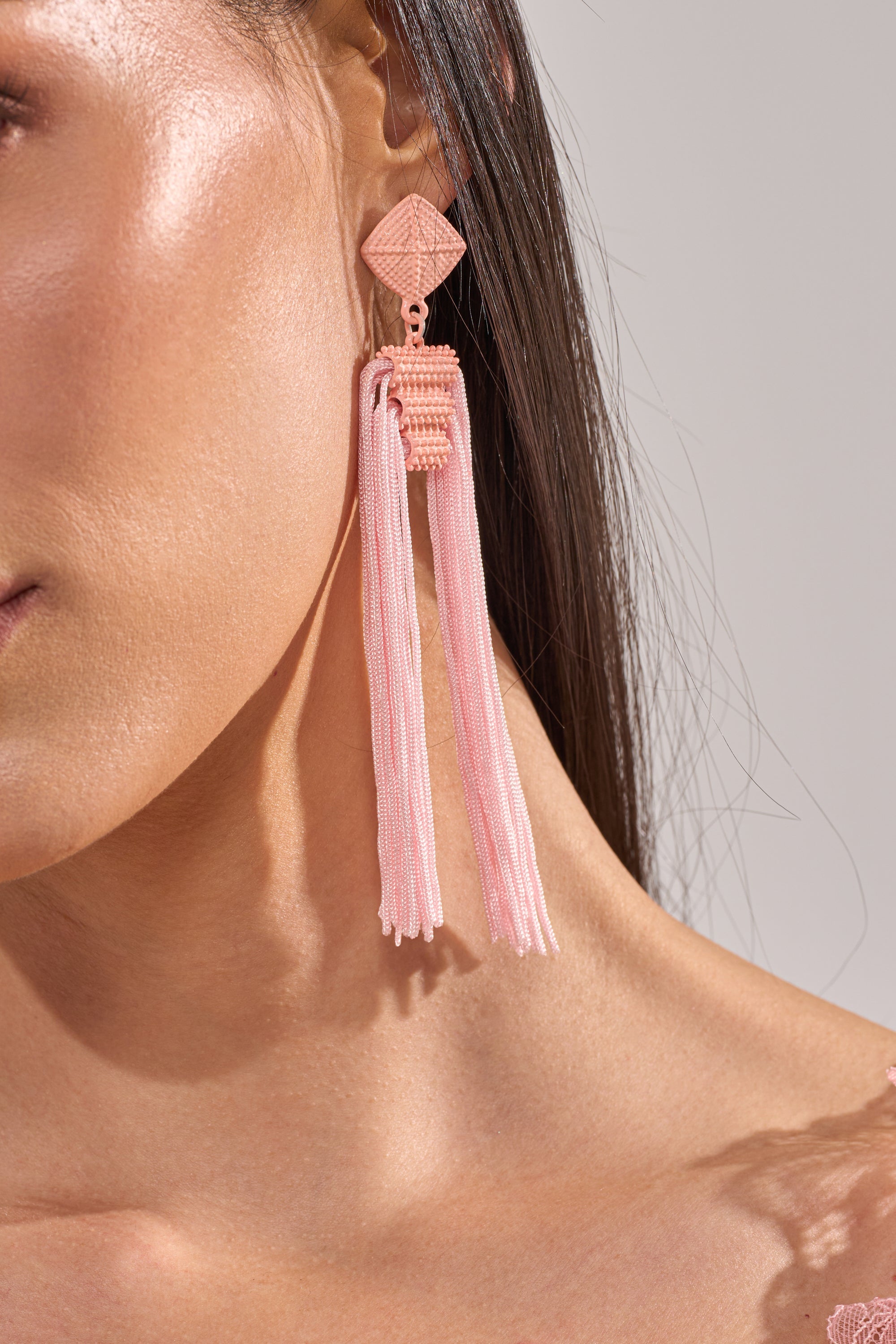 Close-up of a woman's face and shoulder wearing the ASK ME OUT EARRING—pink tassel fringe with braided details. Her straight hair is tucked behind her ear, showcasing the elegant drop design against a neutral background. 4