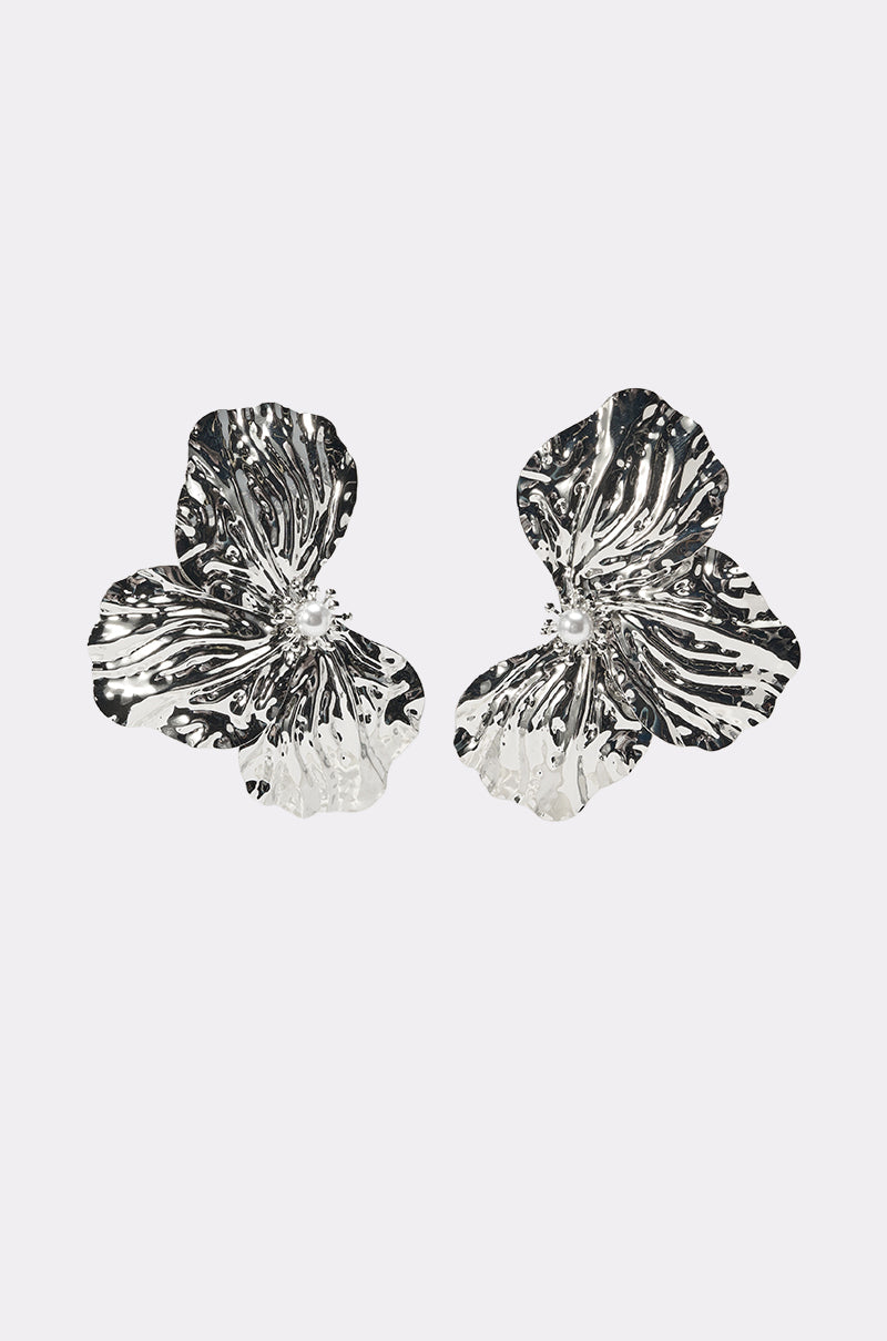 The ON A BOAT EARRING is a pair of oversized, textured silver flower earrings featuring delicate wavy petals and pearl accents, shown against a plain white background. 1