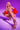 A woman with long blonde hair poses against a purple background, confidently squatting while wearing the AZALEA WANG YEIRA GOLD SANDAL, pearl jewelry, red ruffled sleeves, bejeweled accessories, and chain link embellishments.