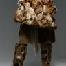 Dressed in a brown ensemble, an individual carries the UPSETTER FAUX FUR TOTE, which features a large, shagadelic design in brown and white faux fur. Complementary tall, furry boots complete the look against a neutral gray background.