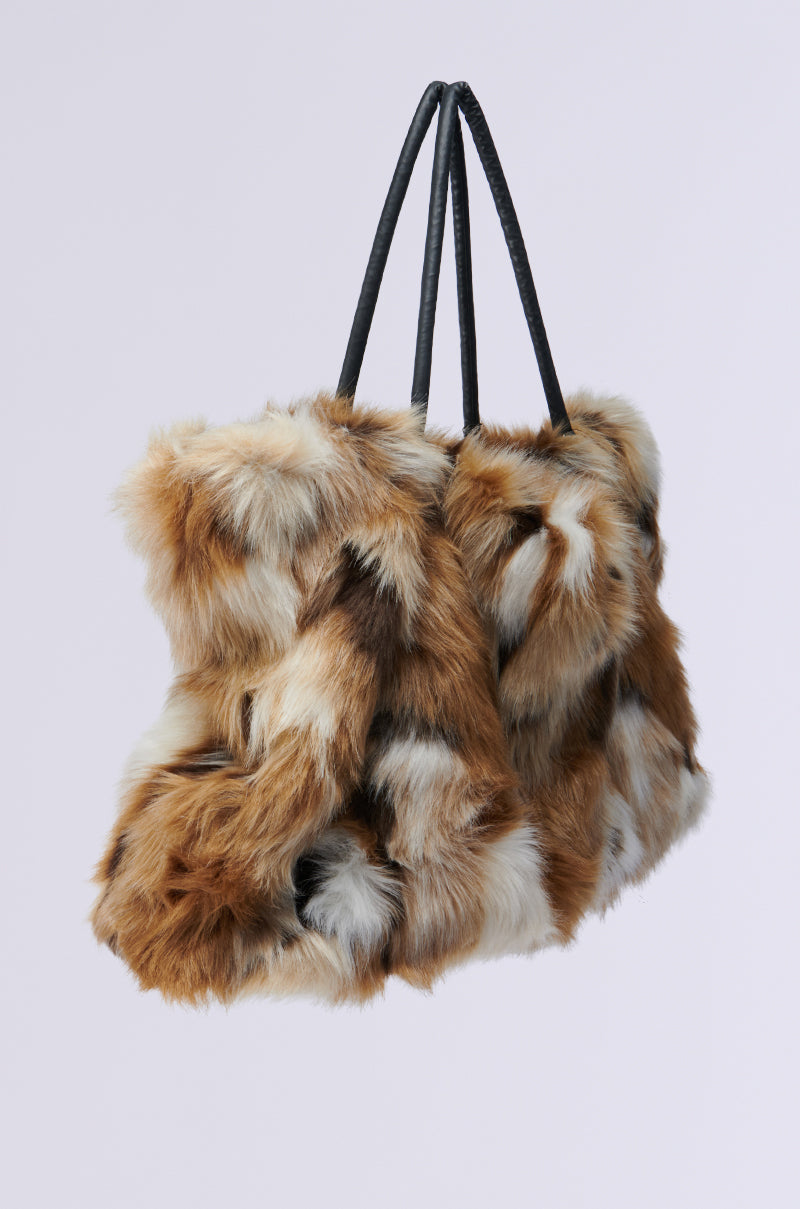 The UPSETTER FAUX FUR TOTE is a shagadelic accessory boasting a patchwork design with brown, white, and black fur-like materials. It features black handles and offers a soft, luxurious texture set against a plain background. 2
