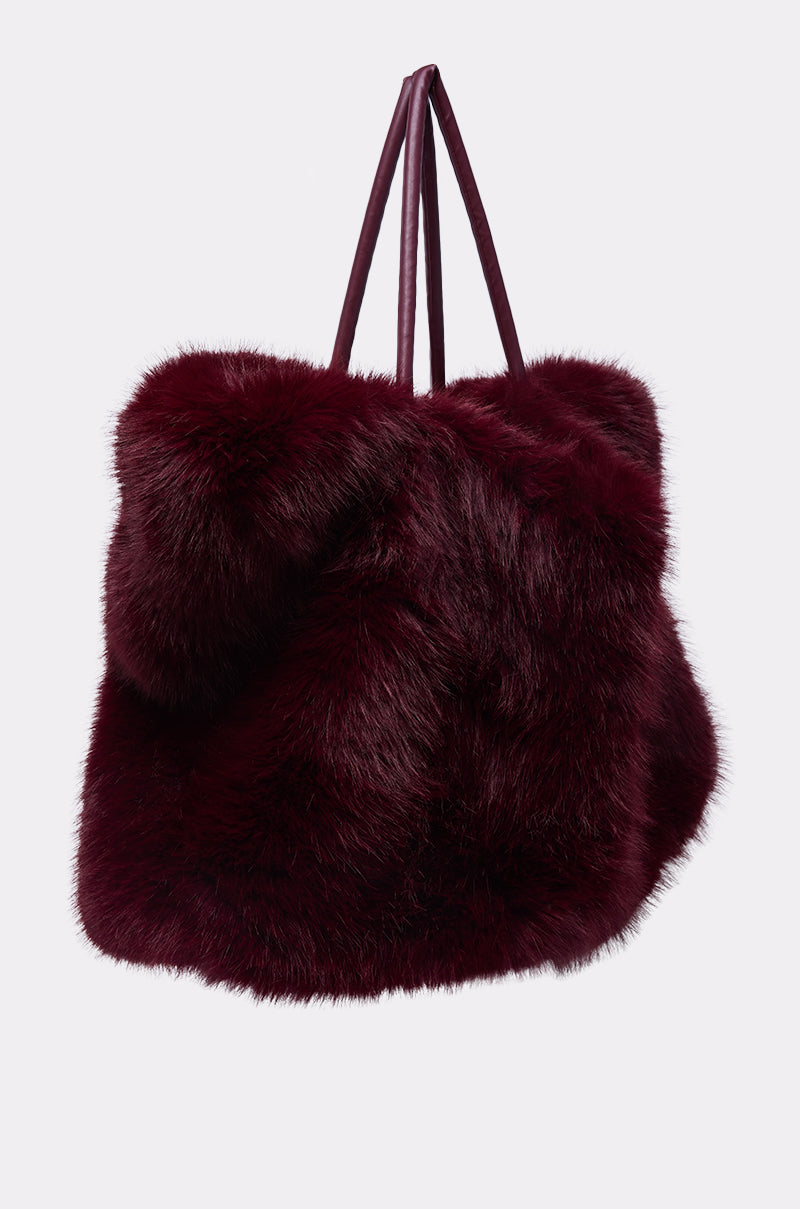 The ALAIA FAUX FUR TOTE, a large plush tote in deep burgundy with matching slim handles, is displayed against a plain light background.