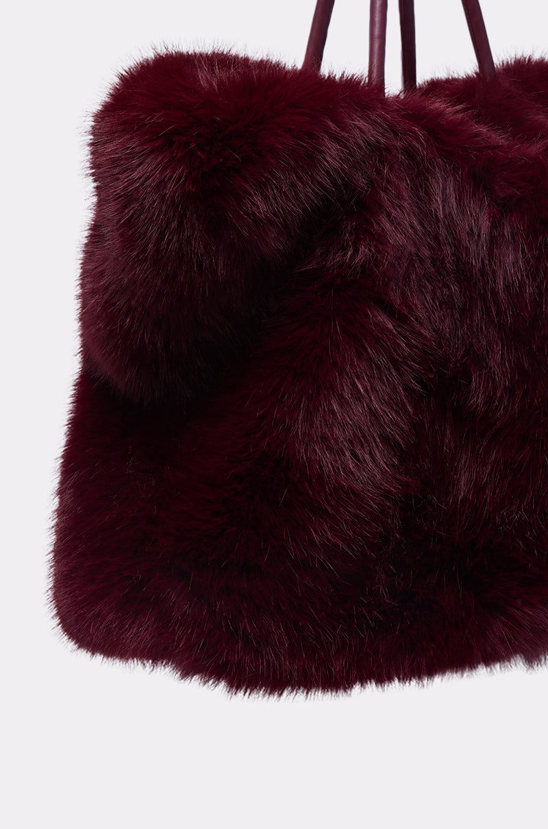 A close-up of the ALAIA FAUX FUR TOTE in plush wine-red faux fur with two handles, displayed against a plain white background.