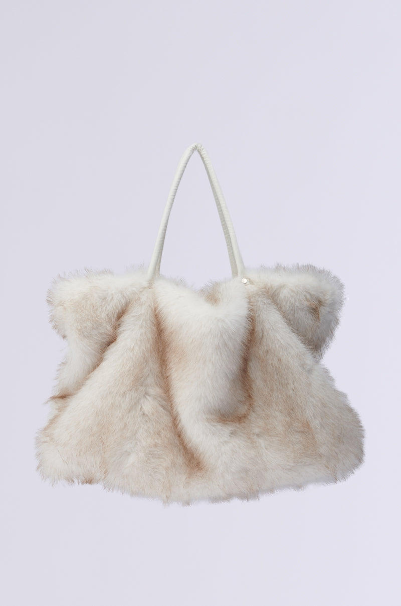 The TOASTIE FAUX FUR TOTE is a spacious, oversized handbag featuring a soft, light beige faux fur texture complemented by white handles. Its plush and luxurious design stands out against the minimalist background.