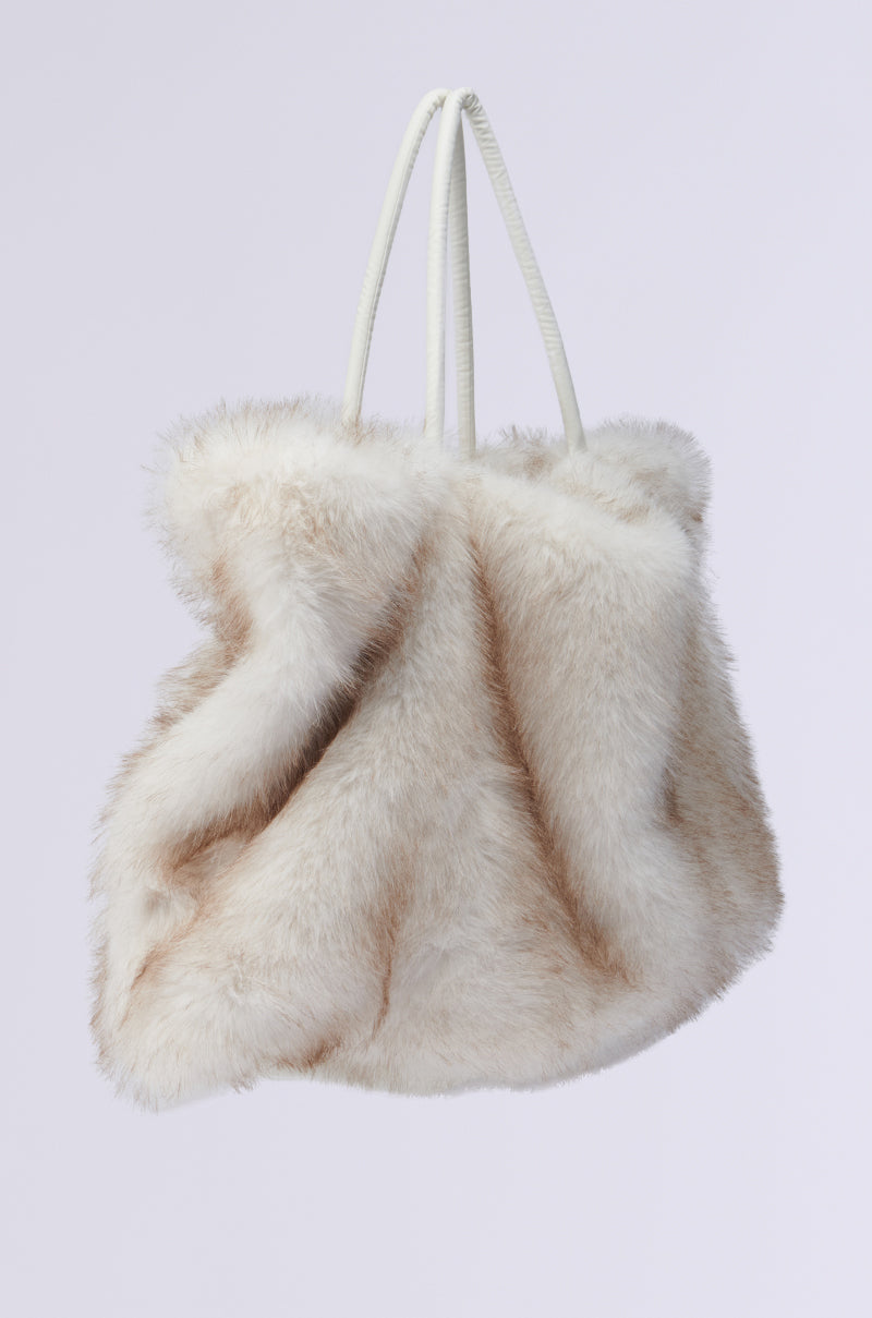 The TOASTIE FAUX FUR TOTE is a luxurious handbag with a soft, fluffy texture in light brown and cream, complemented by white handles. Its plush and voluminous design is beautifully highlighted against a plain white background.