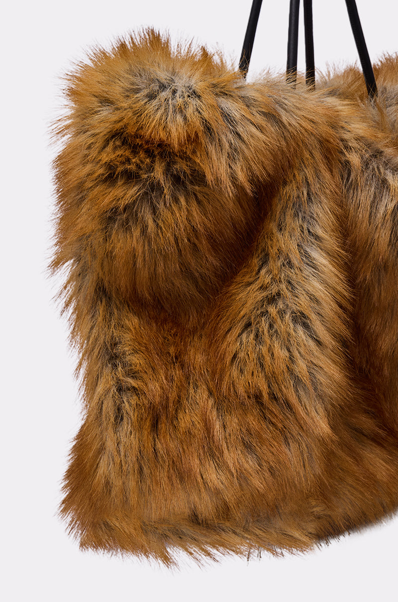 A close-up of the HERE FOR A GOOD TIME FAUX FUR TOTE, featuring its oversized, fluffy brown faux fur and black straps, with the soft, textured surface shown against a plain light background.