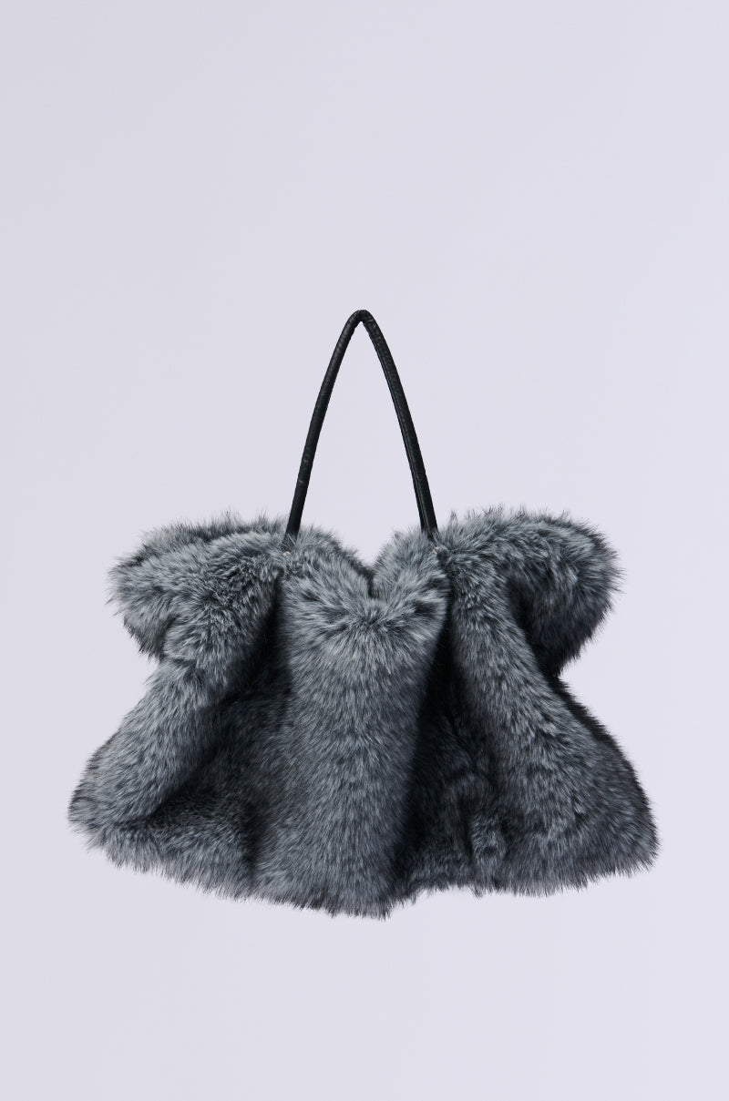Set against a light gray backdrop, the TSUNAMI FAUX FUR TOTE showcases an oversized design with a plush, voluminous texture and a minimalist black handle, radiating warm and cozy vibes.