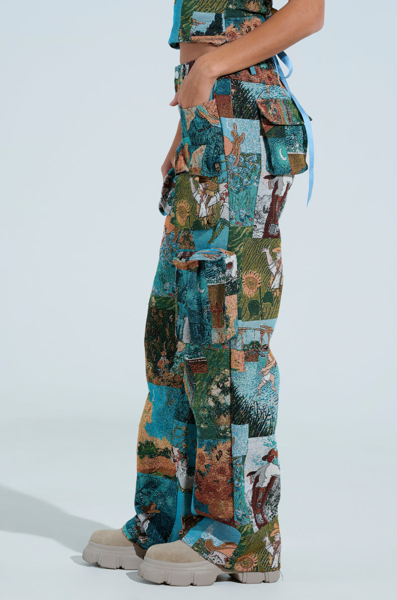 The individual dons the LOCKED AND LOADED TROUSER, showcasing Impressionist-inspired jacquard artwork with nature scenes of plants and animals. Beige chunky shoes complement the outfit against a plain light blue backdrop.