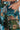 A person wearing vibrant LOCKED AND LOADED TROUSER with a hand in the pocket. The intricate print, inspired by Impressionist artwork, showcases abstract designs in shades of blue, green, orange, and brown.
