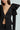 A woman models the stylish, black Mila Fitted Blouse with dramatic puff sleeves and a plunging V-neckline, teamed with pinstriped black pants. The photo is cropped at the shoulders and mid-thigh against a light blue background.
