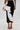 A person wearing the FASHION ICON RUFFLE BANDAGE MAXI SKIRT featuring bold white ruffle details, paired with a round metallic clutch bag and black strappy high-heeled sandals.