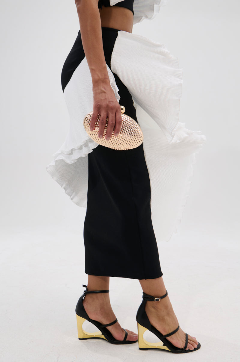 A person showcases the FASHION ICON RUFFLE BANDAGE MAXI SKIRT—a black pleated ruffle skirt with white ruffle accents—paired with black and gold heeled sandals and a small gold mesh clutch, set against a plain white background. 3