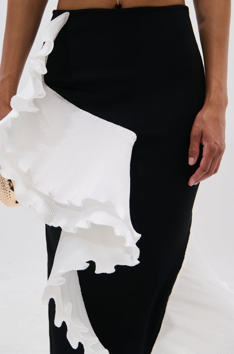 A person wears the FASHION ICON RUFFLE BANDAGE MAXI SKIRT—a high-waisted bodycon design with dramatic, textured white ruffle detailing along one side—shown from waist to knees, with one arm resting at their side. 7