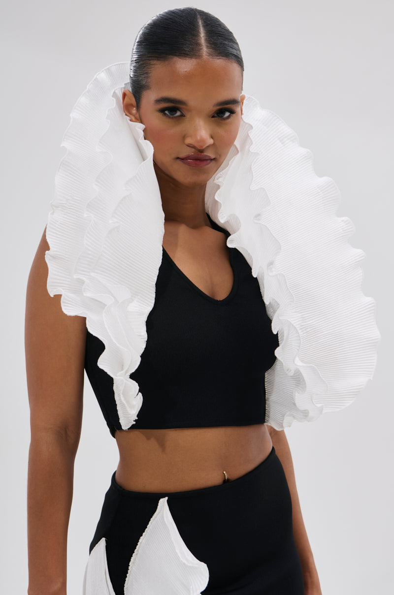 A person wears the FASHION ICON RUFFLE BANDAGE BLOUSE, a black sleeveless crop top with a dramatic, 3D white pleated ruffle collar extending from the shoulders, paired with a high-waisted skirt against a plain light background. 0