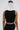 Facing away, a person wears the FASHION ICON RUFFLE BANDAGE BLOUSE—a sleeveless black top with bold, white 3D ruffles fanning out behind their head against a plain light background.