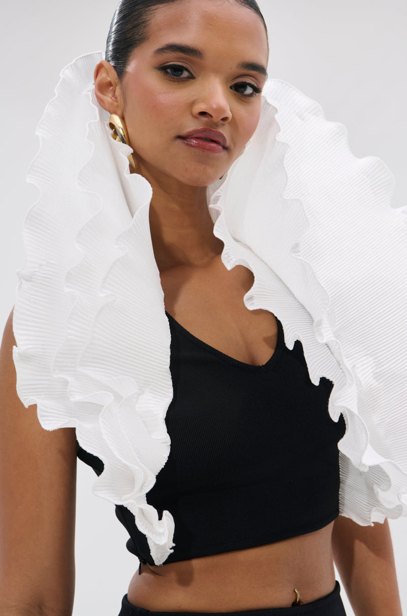 A woman with slicked-back hair models the FASHION ICON RUFFLE BANDAGE BLOUSE—a sleeveless black crop top with a dramatic 3D ruffle collar. She completes the look with bold gold earrings against a simple background. 7