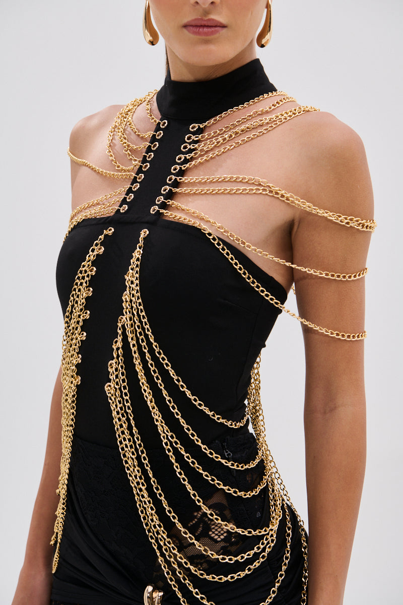 A person wears the CHAINS DRIP BODYSUIT, a sleeveless black piece with a striking silhouette and gold-tone chain details draped over the shoulders, chest, and waist, standing against a plain background. 9