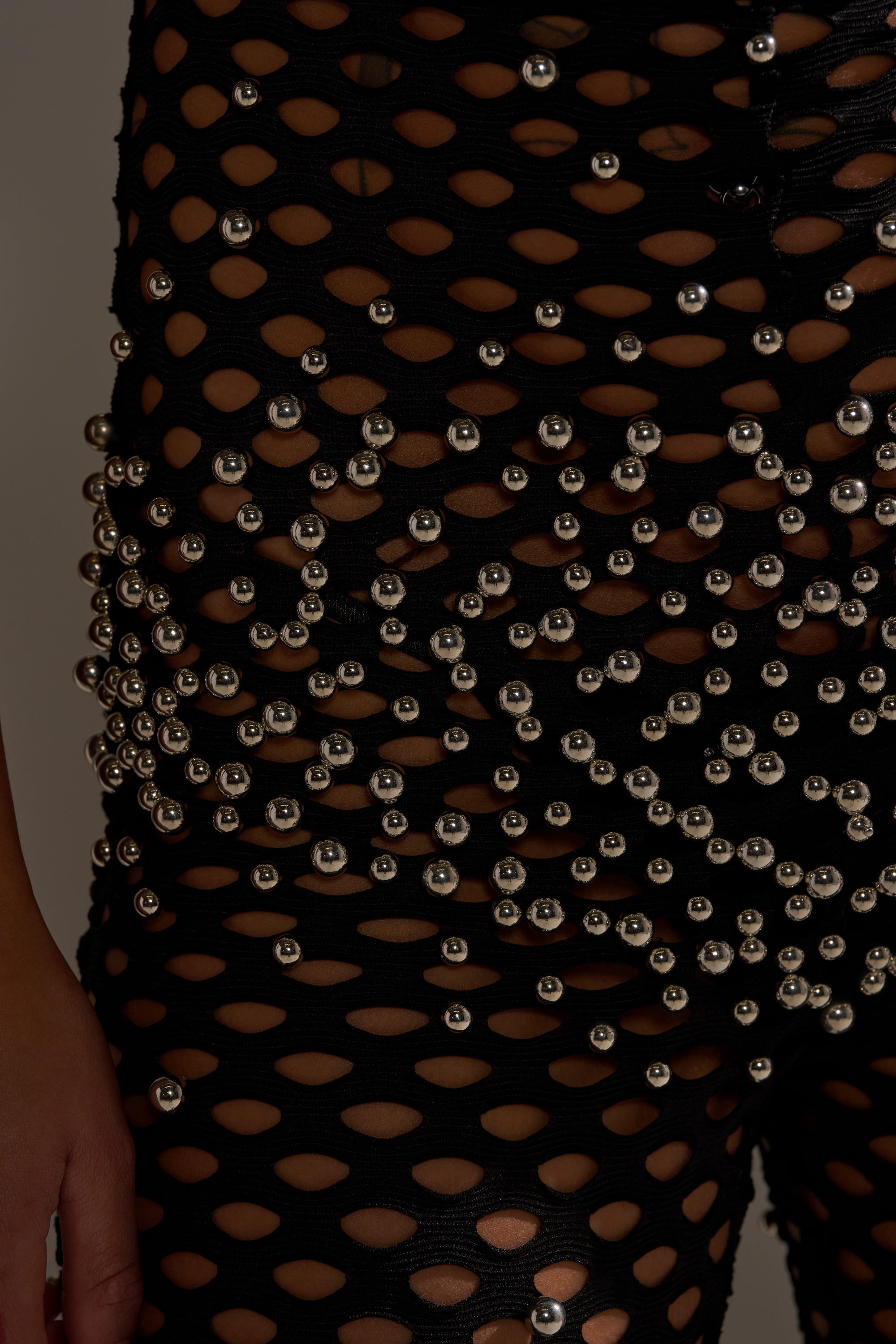 Close-up of a person wearing the COULD NEVER BE ME BEADED MESH JUMPSUIT, featuring black sheer mesh adorned with shiny silver beads. The focus is on the hip and upper thigh, highlighting the revealing design.